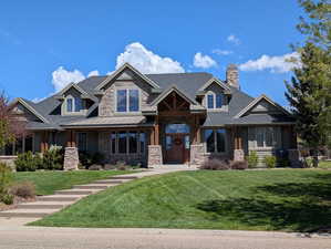 Craftsman inspired home featuring a front lawn, a shingled roof, a porch, stone siding, and a chimney