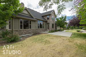 View of front of home with stone siding, a front yard, a shingled roof, a chimney, and entry steps