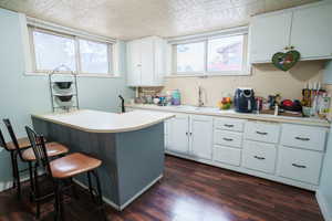 Kitchen featuring light countertops, a kitchen breakfast bar, a peninsula, white cabinetry, and dark wood finished floors