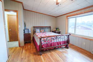 Bedroom with light wood-type flooring, ornamental molding, a ceiling fan, and wooden walls