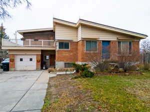 View of front facade featuring driveway, brick siding, a balcony, and an attached garage