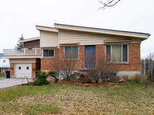View of front of property featuring brick siding, a balcony, driveway, and a garage