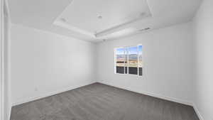 Empty room featuring dark colored carpet and a tray ceiling