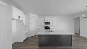 Kitchen with light stone counters, dark wood-style floors, a kitchen island with sink, stainless steel appliances, and two tone cabinets