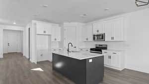Kitchen featuring stainless steel appliances, two tone color scheme, a kitchen island with sink, dark wood-style flooring, and light stone counters