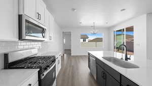 Two tone kitchen featuring stainless steel appliances, two tone color scheme, light wood-type flooring, light stone countertops, and a chandelier