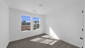 Spare room featuring baseboards and dark carpet