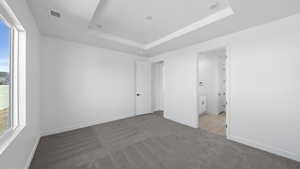 Unfurnished bedroom featuring light colored carpet, a raised ceiling, and ensuite bathroom