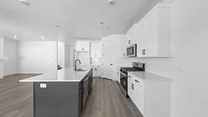 Dual tone kitchen with two tone cabinets, stainless steel appliances, a kitchen island with sink, dark wood-type flooring, and decorative backsplash