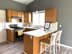 Kitchen featuring a kitchen bar, stainless steel gas range, brown cabinets, and light countertops