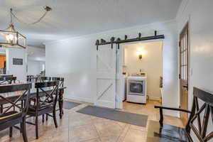 Dining room featuring a textured ceiling, crown molding, a barn door, washer and dryer, and light tile patterned flooring