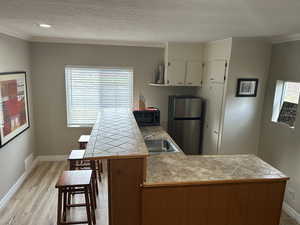 Kitchen featuring crown molding, a textured ceiling, a peninsula, freestanding refrigerator, and a breakfast bar