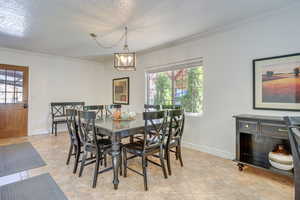 Dining area with a textured ceiling, crown molding, a chandelier, and light tile patterned flooring