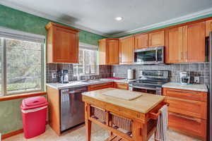 Kitchen with stainless steel appliances, backsplash, brown cabinetry, ornamental molding, and a textured ceiling