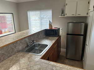Kitchen featuring freestanding refrigerator, black microwave, and white cabinets