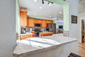 Kitchen with light countertops, stainless steel appliances, a textured wall, tasteful backsplash, and brown cabinetry