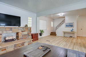 Living room with a textured ceiling, crown molding, wood finished floors, stairway, and a fireplace