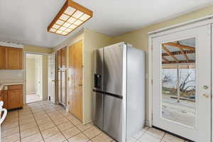 Kitchen with stainless steel fridge with ice dispenser, light countertops, light tile patterned floors, brown cabinets, and range