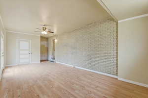 Unfurnished room featuring ornamental molding, brick wall, light wood-style flooring, and a ceiling fan