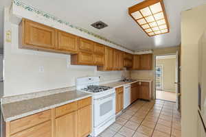 Kitchen featuring white appliances, light countertops, light tile patterned floors, and brown cabinetry
