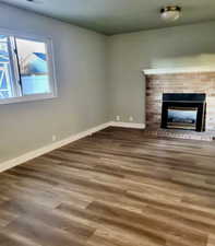 Unfurnished living room featuring a brick fireplace and dark wood-style floors