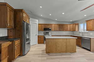Kitchen with stainless steel appliances, brown cabinets, lofted ceiling, light wood-style flooring, and a center island
