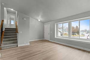 Unfurnished living room with stairway, light wood finished floors, lofted ceiling, and a textured ceiling