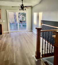 Corridor with light wood-style floors, a textured ceiling, and lofted ceiling
