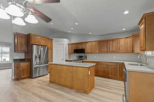 Kitchen with lofted ceiling, stainless steel appliances, a kitchen island, light wood finished floors, and brown cabinetry