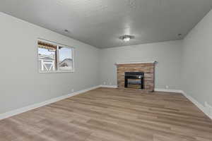 Unfurnished living room featuring a fireplace, light wood-style flooring, and a textured ceiling