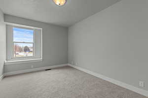 Carpeted empty room with a textured ceiling and baseboards