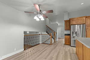 Kitchen featuring stainless steel fridge, brown cabinetry, a ceiling fan, light wood finished floors, and dark stone countertops