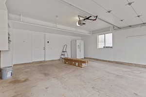 Garage with white refrigerator with ice dispenser and a garage door opener