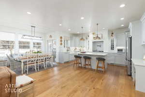 Kitchen with pendant lighting, a kitchen bar, light wood-style floors, light stone countertops, and high end refrigerator