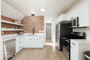 Kitchen with open shelves, stainless steel appliances, white cabinets, vaulted ceiling, and light wood-style floors