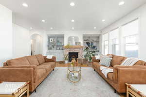 Living area with built in features, arched walkways, a fireplace, wood finished floors, and recessed lighting