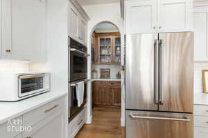 Kitchen featuring appliances with stainless steel finishes, decorative backsplash, white cabinets, light wood-type flooring, and light stone counters
