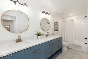 Bathroom featuring shower / bathtub combination with curtain, double vanity, and light tile patterned floors