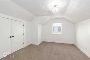 Additional living space featuring vaulted ceiling and light colored carpet