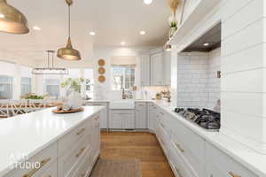 Kitchen featuring tasteful backsplash, pendant lighting, stainless steel gas cooktop, light wood-style floors, and light stone countertops