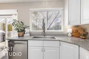 Kitchen with white cabinetry, stainless steel dishwasher, dark stone counters, and healthy amount of natural light
