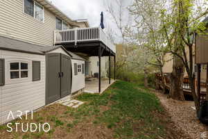 View of green lawn featuring a wooden deck, a patio, and an outdoor structure