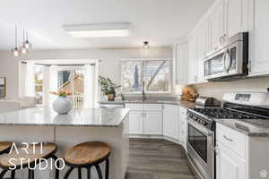 Kitchen with appliances with stainless steel finishes, a breakfast bar area, white cabinetry, and light stone countertops