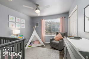 Bedroom featuring a crib, dark wood-type flooring, a ceiling fan, and a closet