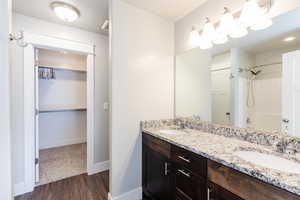Full bath with a walk in closet, double vanity, washtub / shower combination, and dark wood-style floors
