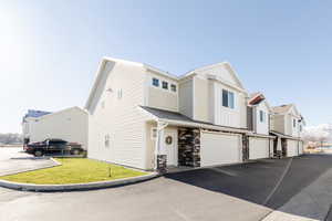 View of front of property featuring a garage, a residential view, board and batten siding, driveway, and stone siding