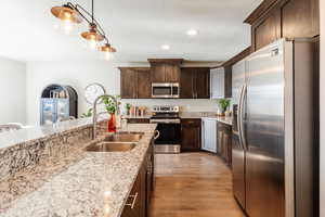 Kitchen featuring appliances with stainless steel finishes, dark brown cabinetry, decorative light fixtures, light stone counters, and recessed lighting