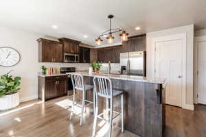 Kitchen featuring dark brown cabinetry, a breakfast bar area, appliances with stainless steel finishes, an island with sink, and recessed lighting