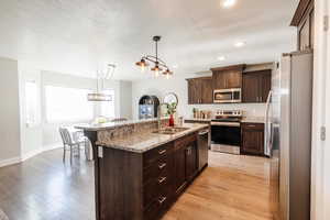 Kitchen featuring appliances with stainless steel finishes, dark brown cabinets, light stone countertops, a textured ceiling, and light wood-style floors