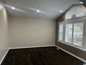 Empty room featuring dark carpet, vaulted ceiling, and recessed lighting